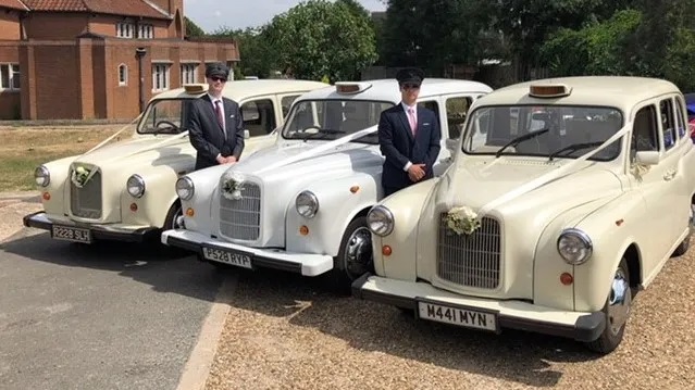 Three iconic classic London taxis Cabs in white and ivory with their fully uniformed chauffeurs standing by the vehicles