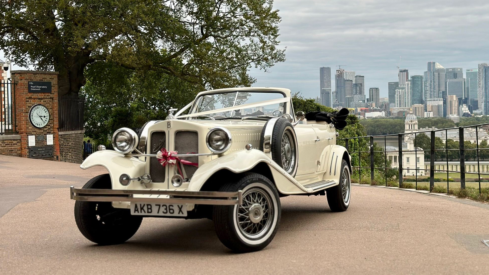 Ivory vintage Beauford convertible with roof down decorated withivory ribbon and a burgundy bow at a local Bexleyheath wedding with view of the city of London in the background.