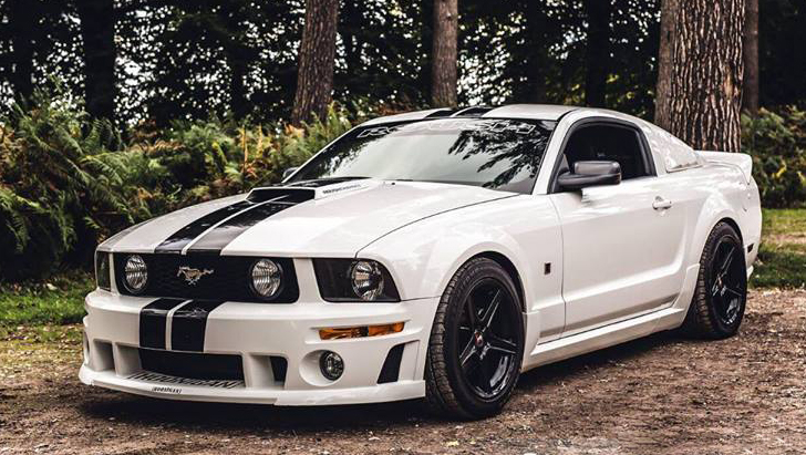 Modern White Mustang with black wheels parked in a forest path with trees in the background.