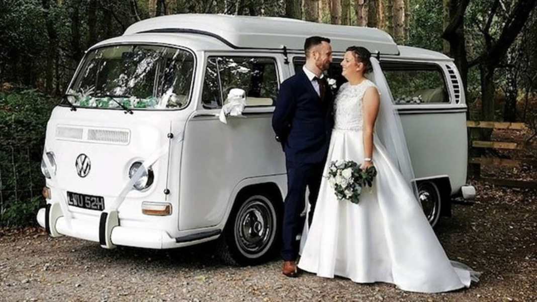Classic Volkswagen Campervan splitscreen with Bride and Groom standing in front of the vehicle looking at each others.  Vehicle is parked in the garden of a Newquay wedding venue.