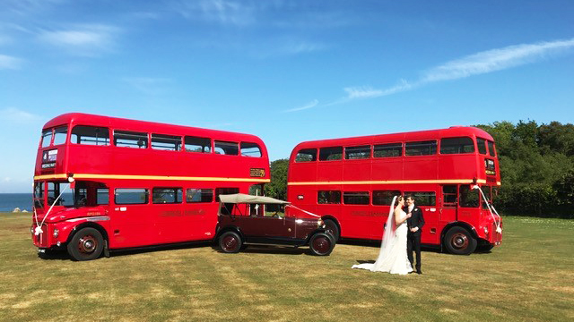 Two Vintage Red Routemaster buses with a vintage Burgundy car in Cerne Abbas. Bride and Groom are standing in front of the vehicles