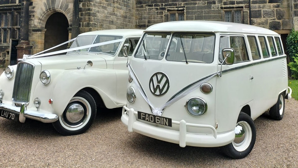 Classic Volkswagen Campervan and a classic 7-seater Austin Princess limousine in white decorated with white ribbons. Vehicles are parked in front of a local Bamber Bridge wedding v