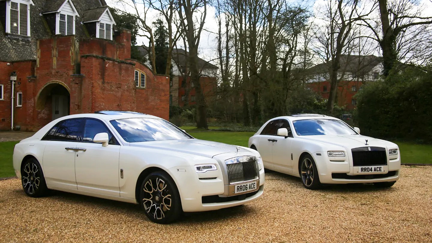 Two Modern White Rolls-Royce Ghosts with their large chrome grill decorated with the famous spirit of ecstasy mascot on top.