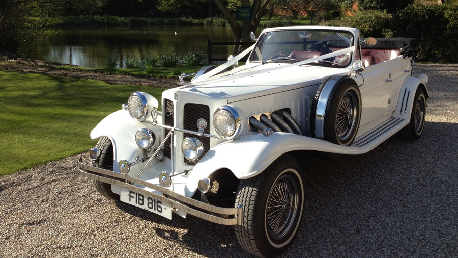 Vintage Beauford convertible with roof down decorated with traditional white wedding ribbons across its bonnet at a local Hitchin park. Spare wheel mounted on side skirt
