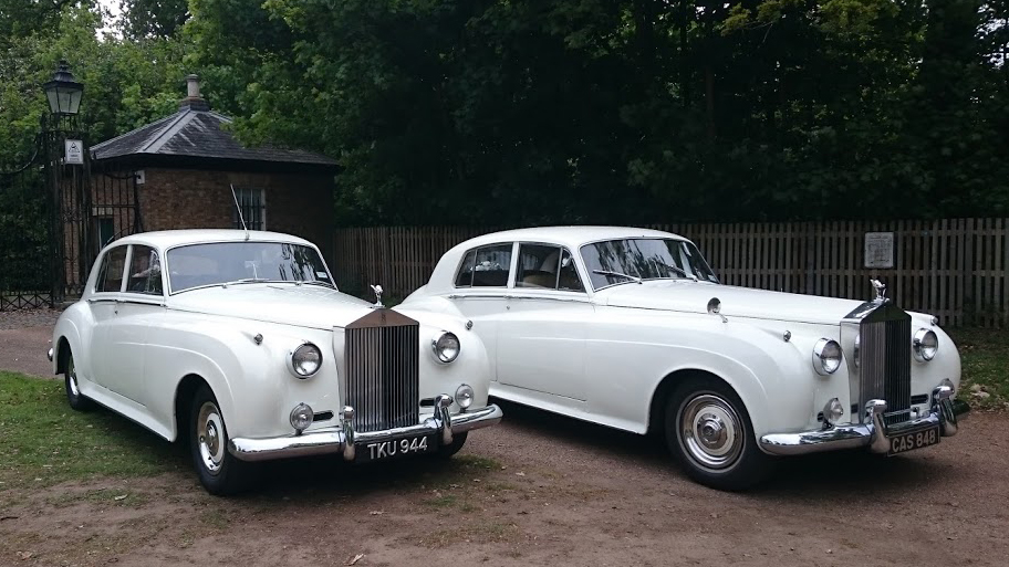 Two identical white Classic Rolls-Royce Silver Clouds with large chrome front grill and spirit of ecstasy mascot on top