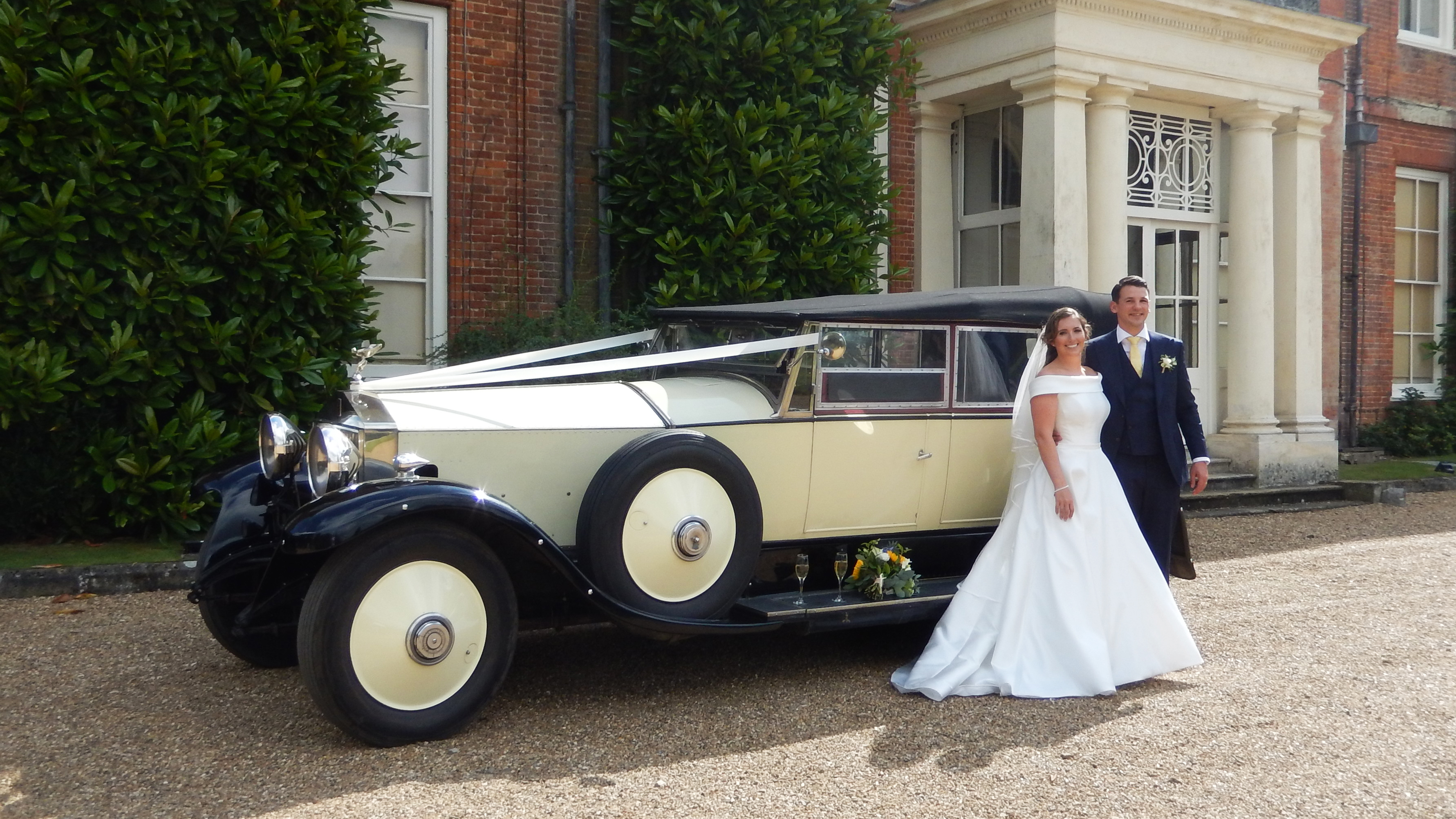 Vintage Rolls-Royce convertible with roof up decorated with traditional white wedding ribbons across its bonnet at a local Sunbury-on-Thames wedding venue. Spare wheel mounted on s