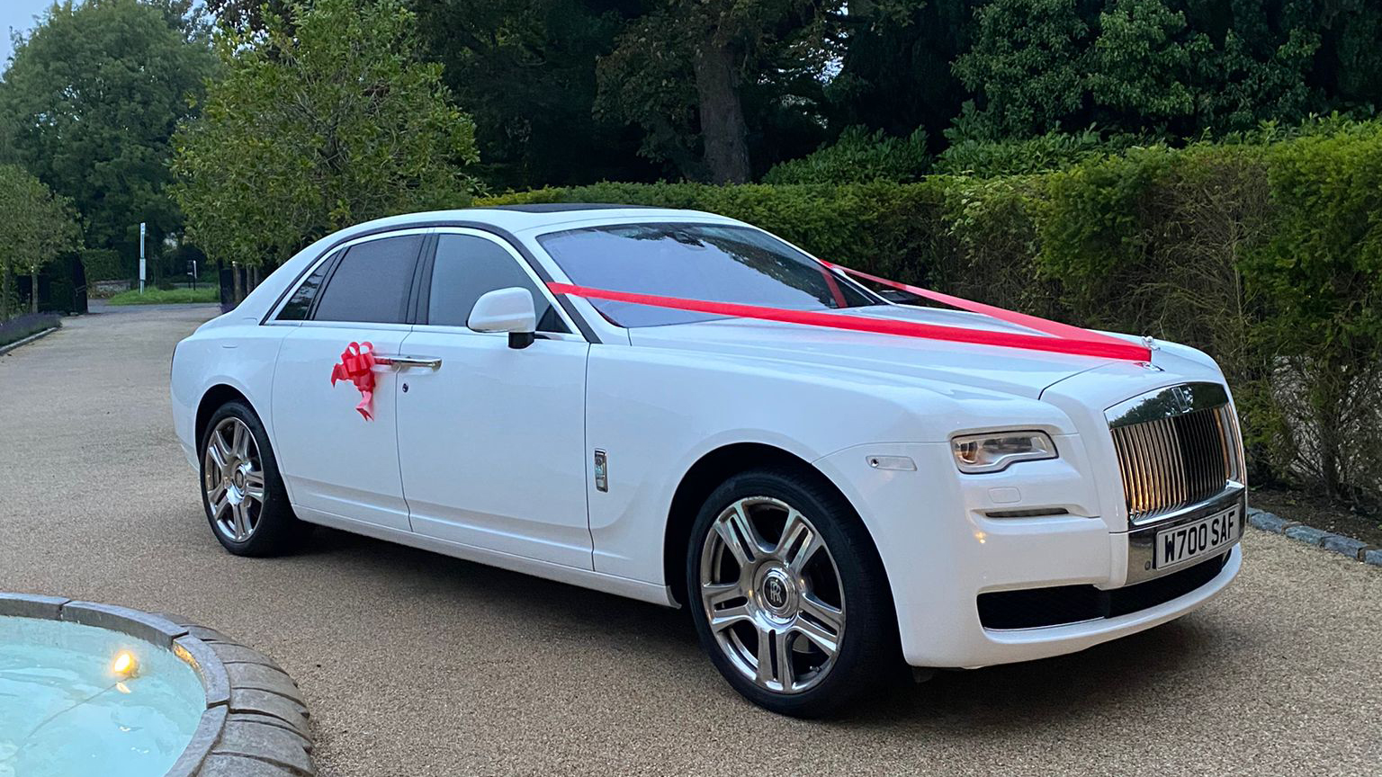 A modern white Rolls-Royce Ghost with Red Ribbons and bows on its door handle in Guildford.
