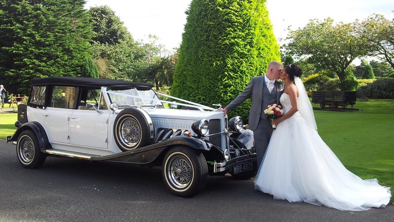 Bride and Groom kissing outdoor at a popular Sheffield wedding venue. A White Beauford Convertible shown in the background