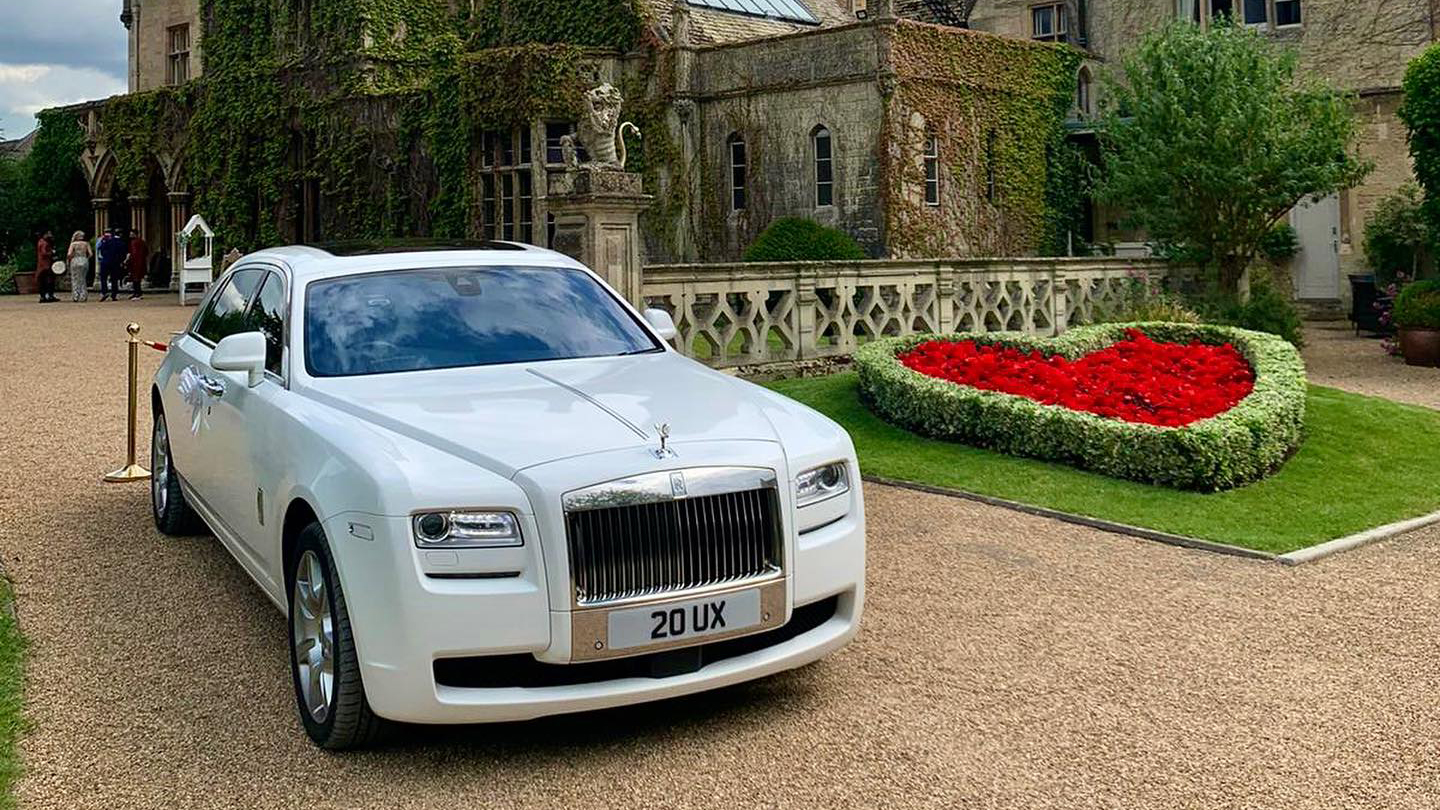 A White Rolls-Royce Ghost parked in front of a wedding venue in Enderby. Red love-heart made of flowers in the background.