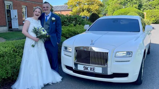 Happy couple standing next a modern white Rolls-Royce after their wedding ceremony in Shropshire