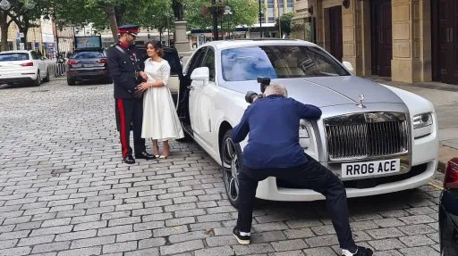 Bride in a white dress and Groom in his military uniform having photos taken by their photographer by the Rolls-Royce they've hired