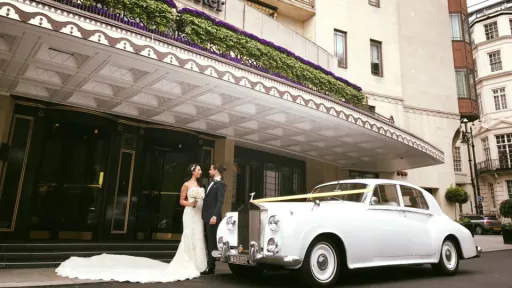 Bride and Groom in Front of the Dorchester Hotel in London with Classic Rolls-Royce Silver Cloud decorated with Ivory Ribbons