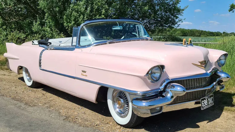 Pink American Cadillac Convertible with roof down, large white banded whitewall tires parked on the side of the road in the Basildon countryside