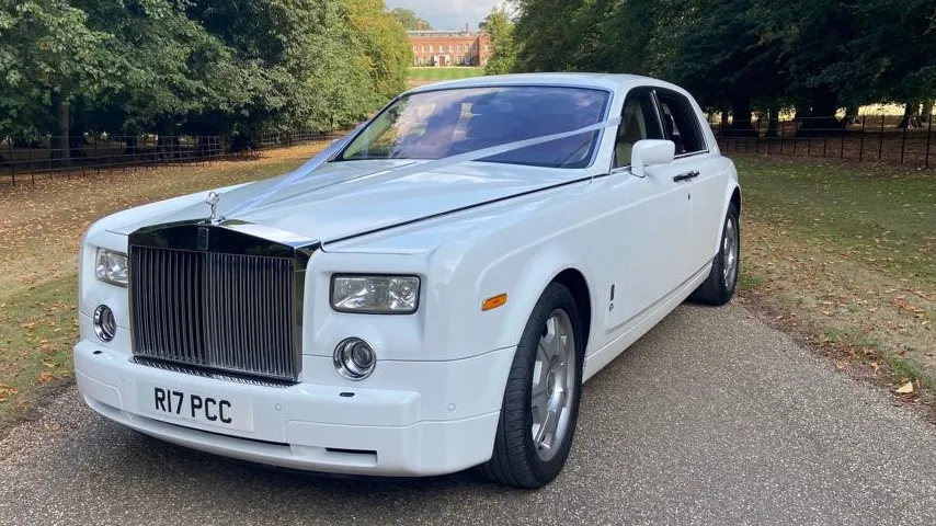 White Rolls-Royce Phantom dressed with traditional V-shape Ribbon accros its front bonnet parked across a path in a park