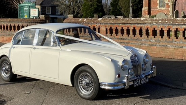 Side view of classic Jaguar in front of Church with White V-Shape Wedding Ribbon Decoration on the bonnet