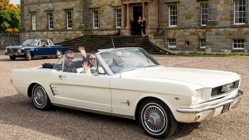 Side view of Cream Classic Ford Mustang Convertible with roof open and wedding ribbons