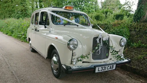 Side view of Ivory Classic Taxi Cab in Cornwall with White Ribbons and flower decoration on front bonnet and old fashion Orange Taxi sign illuminated on Roof