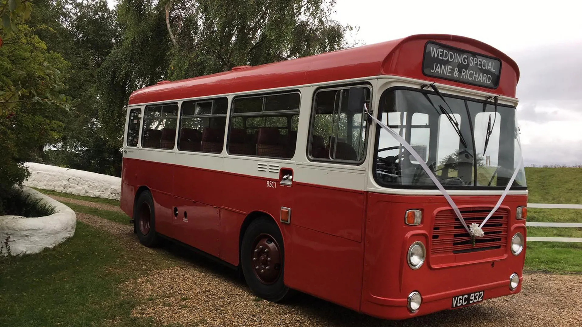 Red Single Decker bus with White Ribbons entering wedding venue