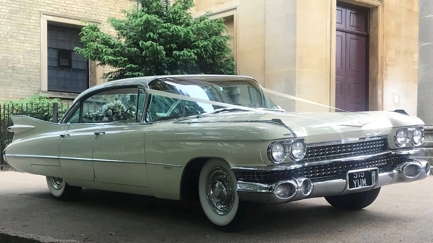 Classic American Cadillac standing in front of the wedding venue with white Ribbons. Car has white wall tires and chrome bumpers