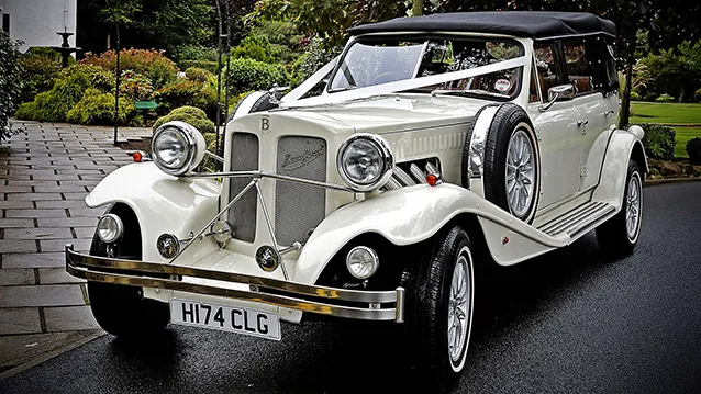 Ivory vintage style Beauford with black soft top roof decorated with White ribbons in front of a wedding venue in Ayr