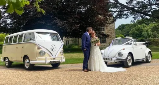 VW Campervan and Beetle decorated with ribbons waiting for bride and groom. Both vehicle are in a matching white and cream coloured. The Beetle has its roof open