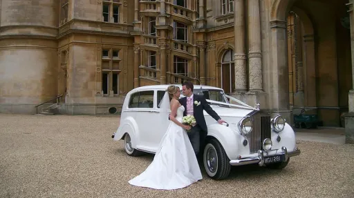 White Rolls-Royce Silver Wraith hired for wedding in Hertfordshire. Car is decorated with ribbons. Bride and Groom standing by the vehicle for photos.