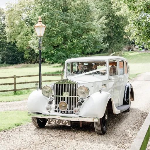 White vintage rolls-Royce Limousine entering Hampshire wedding venue with Bride and Groom. Car is decorated with white ribbons