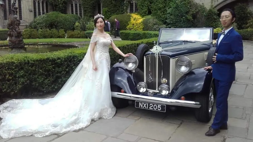 Vintage Convertible Wedding Car decoratedwith white ribbons. Bride and Groom standing by the car for photos