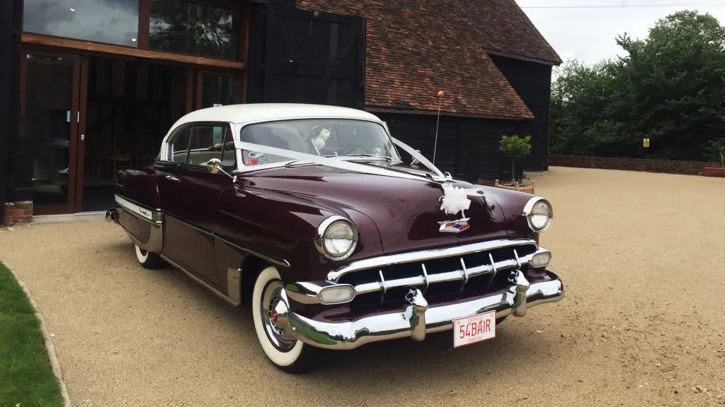 Classic American Chevrolet Belair in Burgundy in front of wedding barn dressed with white Wedding Ribbons