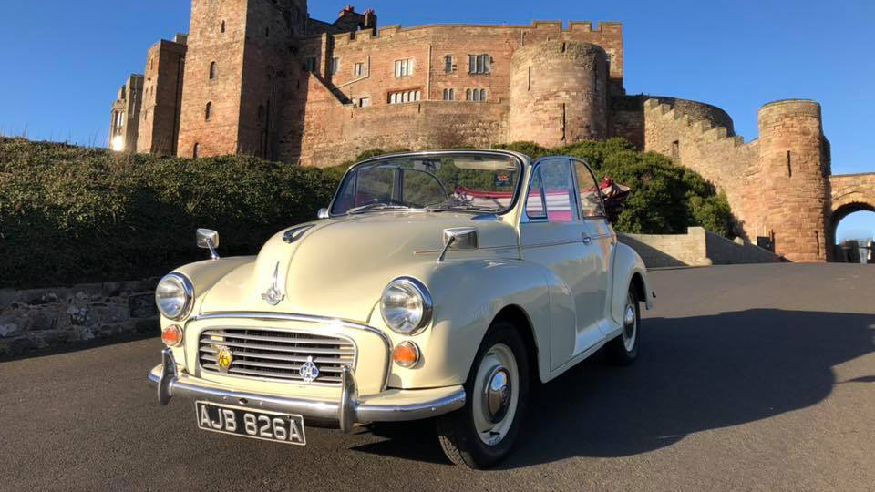 Ivory Convertible Classic Morris Minor with roof open. Castle shown in background