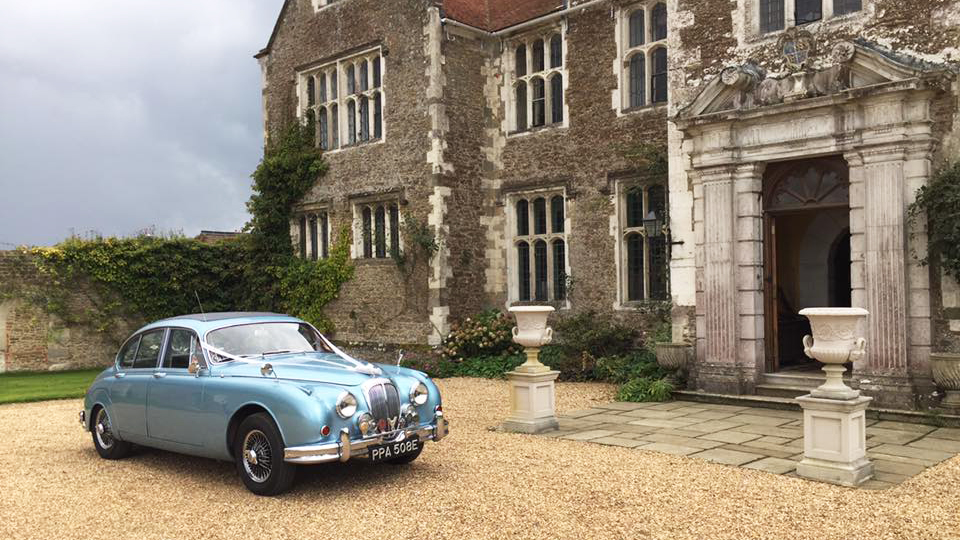 Blue Classic Daimler Saloon Car dressed with white ribbons in front of wedding venue