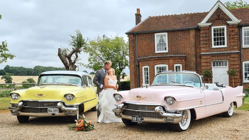 Two Cadillacs in Pink and Yellow at a wedding with bride and groom kissing in the middle of the cars.