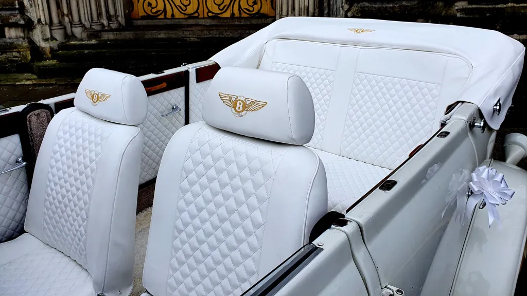 Interior photo of the Beauford with roof open showing the white interior leather seats with Gold Bentley Logos opn headrest