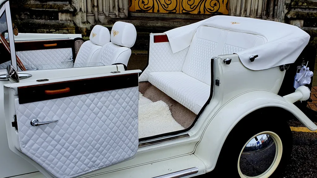 Rear Door of Beauford is open to show large leg room in the rear passengers seats, white carpet  and white leather interior