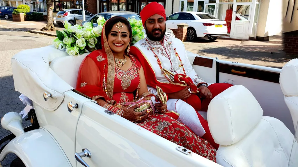 Bauford with roof down and Asian couple having their photo taken. both Bride and Groom are wearing traditionial Asian wedding outfits