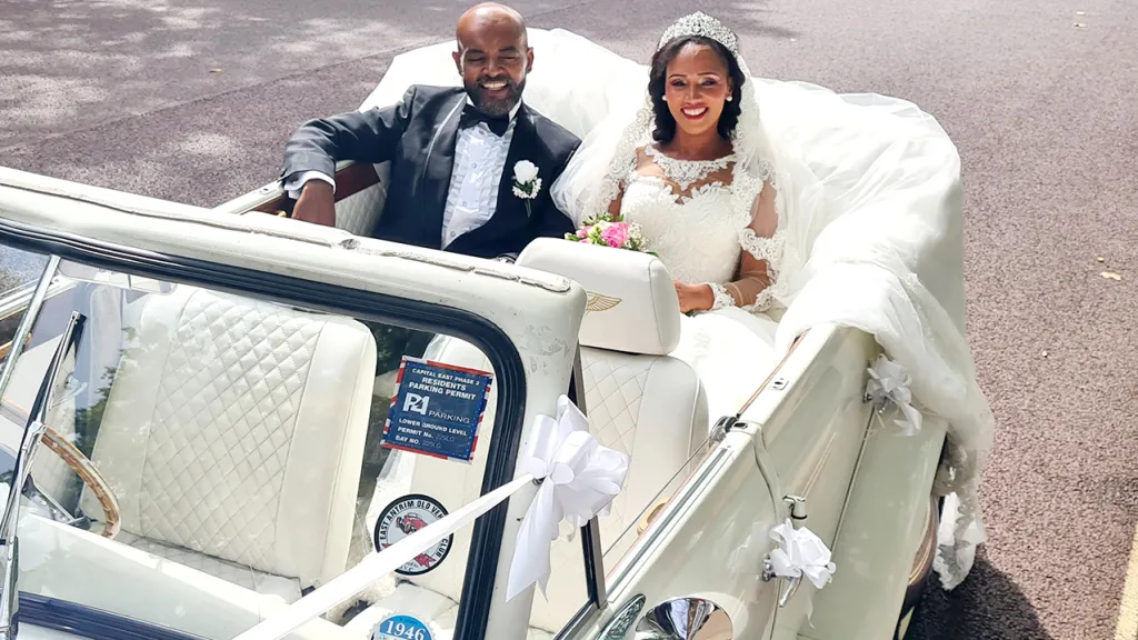 Couple seated in rear bench seat of Beauford. Groom wearing a dark suit and bride a White wedding dress