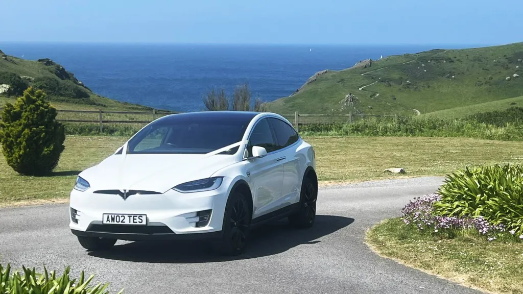 White Tesla driving on coastline. View of the sea in the background