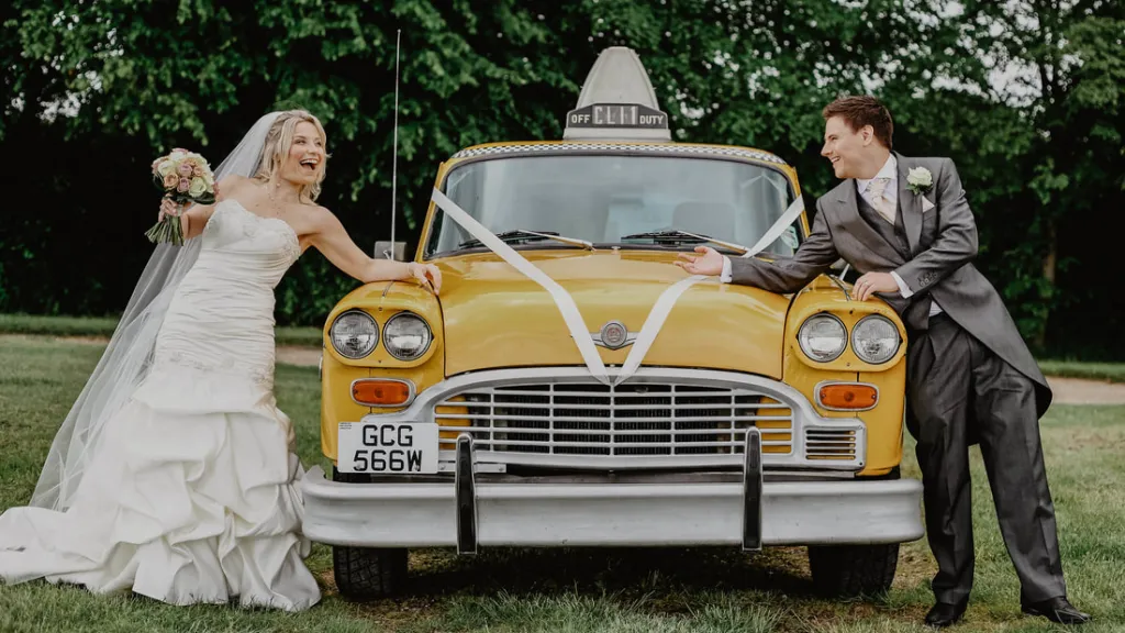 Yellow Cab decorated with wedding ribbons. Bride and groom on either side of the vehicle