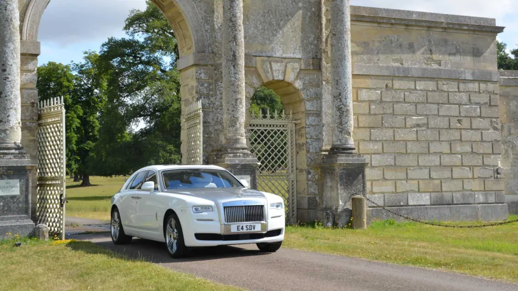 White Rolls-Royce Ghost with silver bonnet and white ribbons entering wedding venue