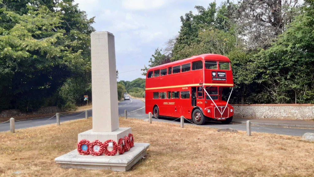 Red Double Decker Routemaster bus decorated with white ribbons driving to wedding venue