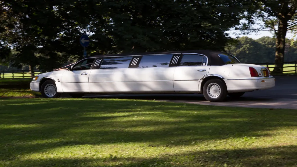 White with black roof Stretched Lincoln Limousine leaving wedding venue