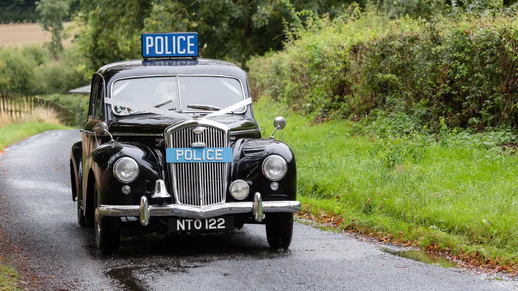 Black classic Wolseley with Blue police sign on its roof and front grill decorated with white ribbons