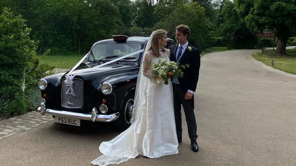 Classic Black Taxi Cab dressed with White ribbons. Bride and Groom posing for photos in a park.