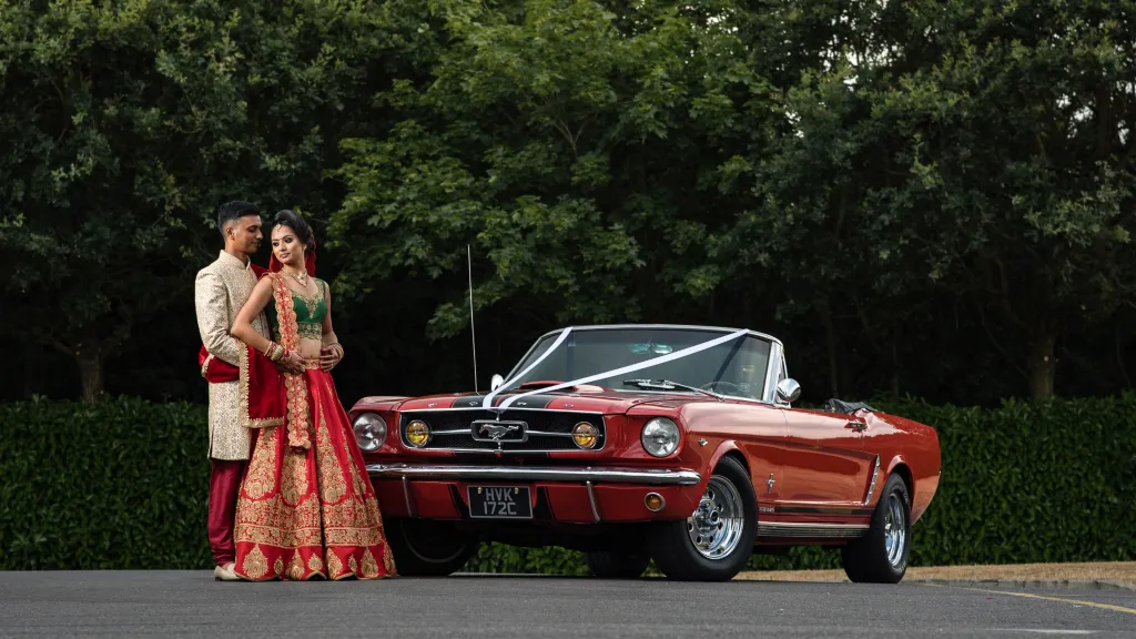 Classic Red Ford Mustang Convertible with roof open and Asian Bride and Groom standing in front of the vehicle