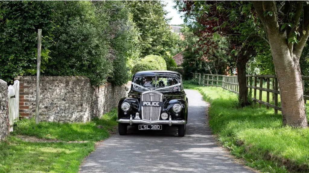 Black Wolseley dressed with white ribbons entering wedding venue. Chauffeur can be seen inside the vehicle