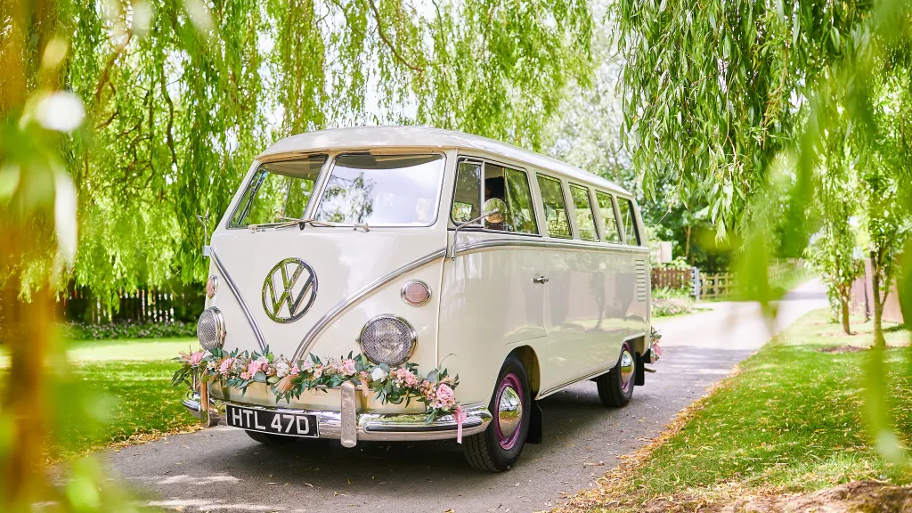 Ivory Classic VW Campervan Splitscreen in a park decorated with wedding flowers on front bumper
