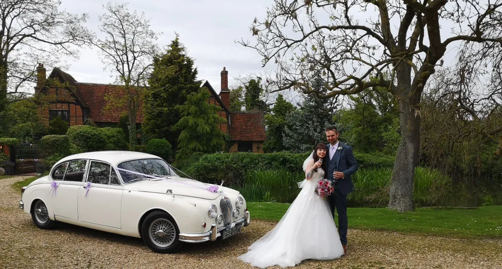 Ivory Classic Jaguar Mk2 at a wedding venue with Bride and Grom standing in front of the vehicle