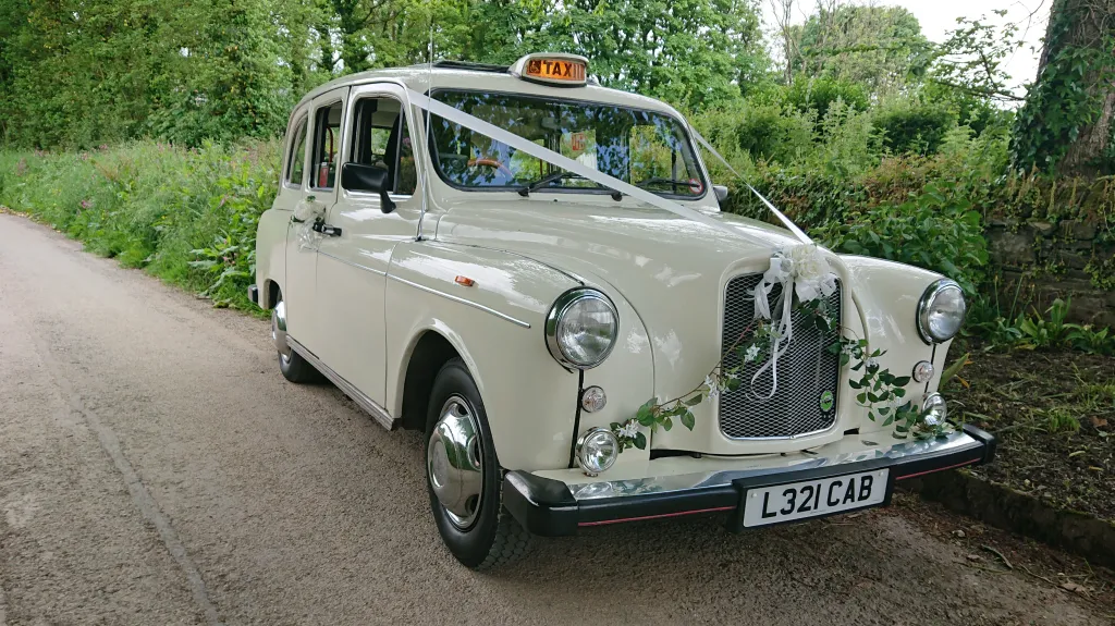 Classic white Taxi Cab decorated with ribbons and wedding flowers on its front grill