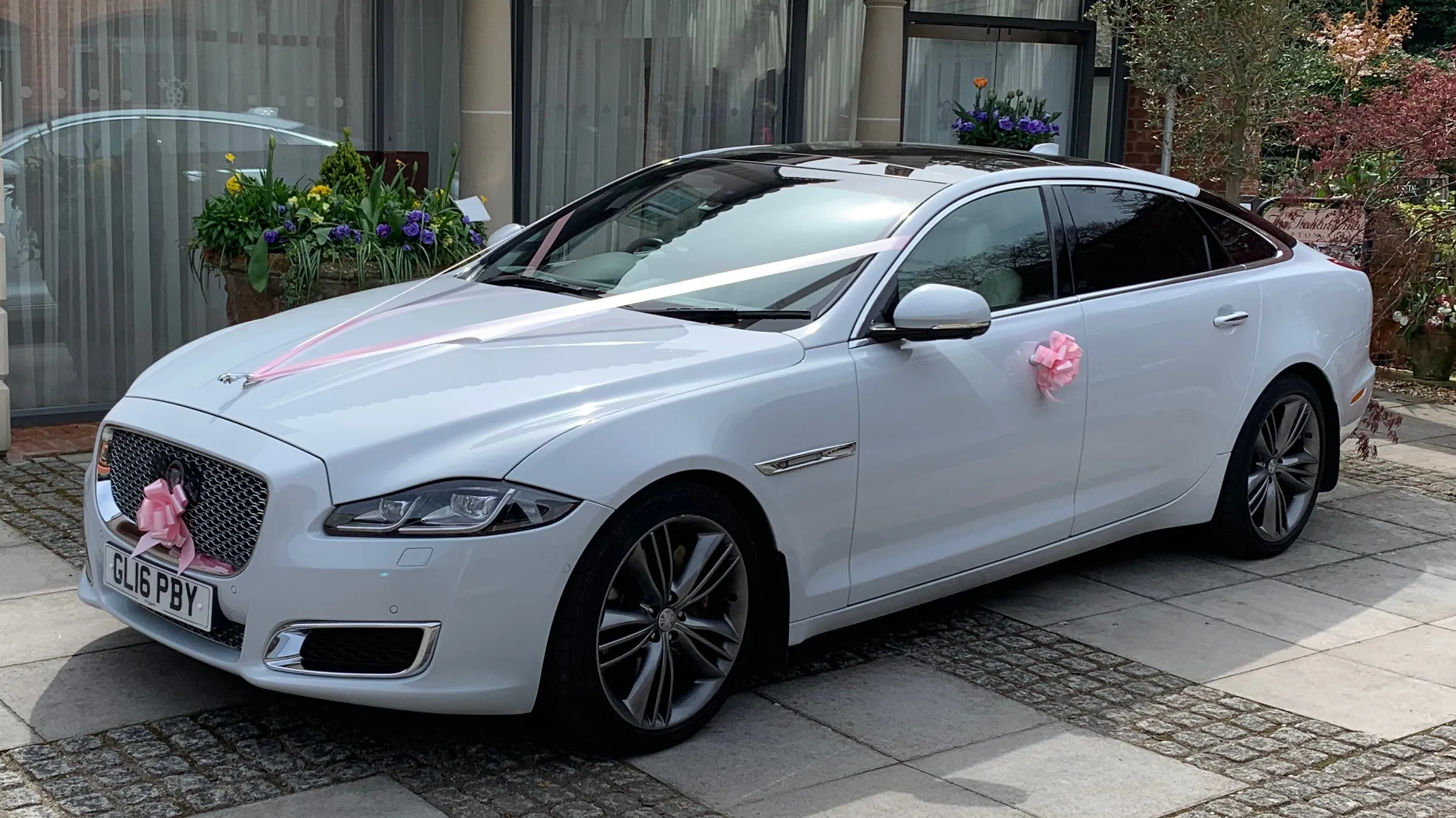 Side view of a White Jaguar XJ decorated with ribbons in front of wedding venue