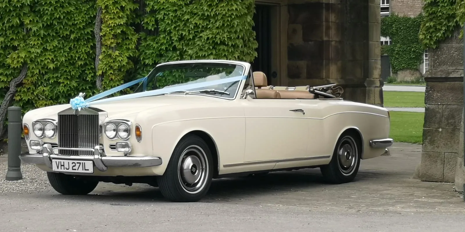 Ivory Classic Rolls-Royce Corniche with roof down and dressed with white ribbons entering the wedding venue